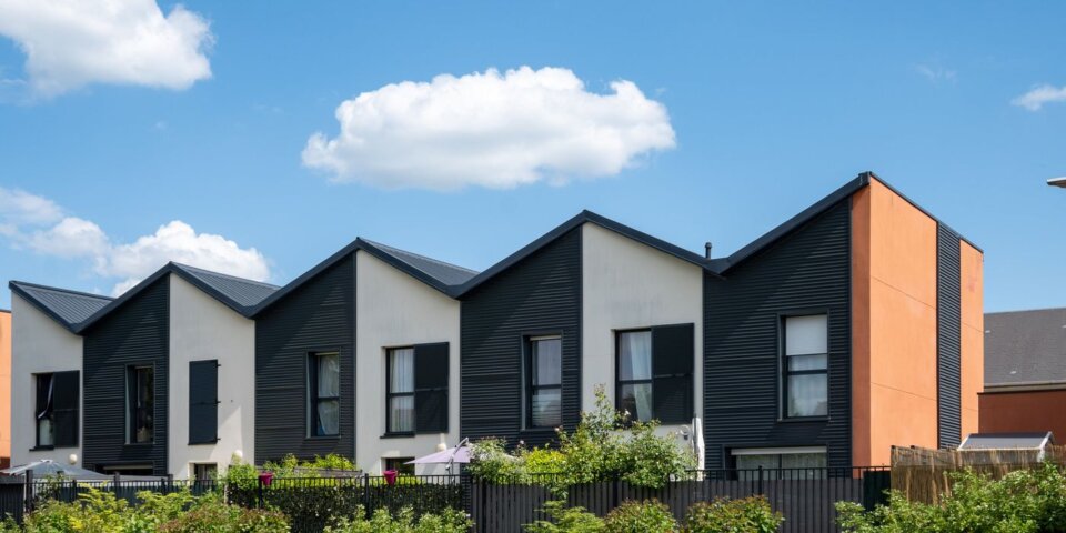 Maisons neuves en bande aux façades sombres et aux toits à pignons, sous un ciel bleu (illustration du PTZ 2027)